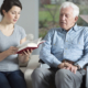 senior home care services provided by an aide reading a senior man a book