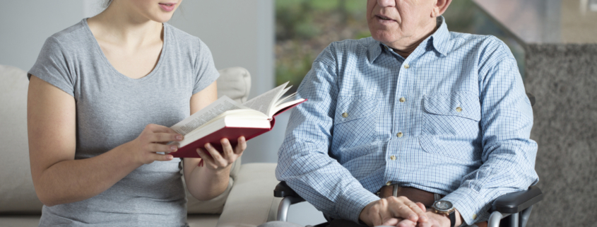 senior home care services provided by an aide reading a senior man a book