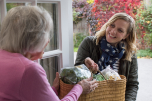 A caregiver handing groceries to senior woman, part of our professional home care services in Port Acres.