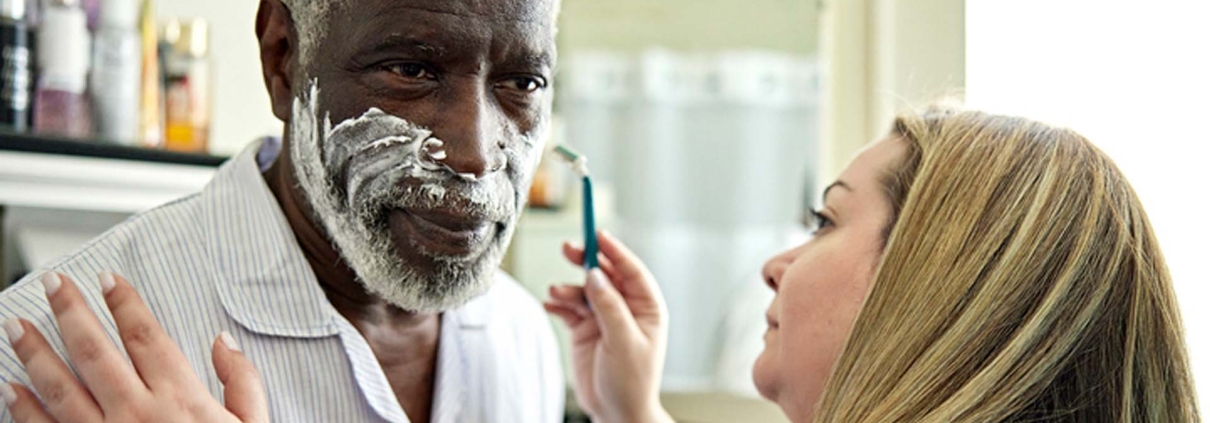 Caregiver woman shaving a senior male as she provides personal care services in Beaumont.