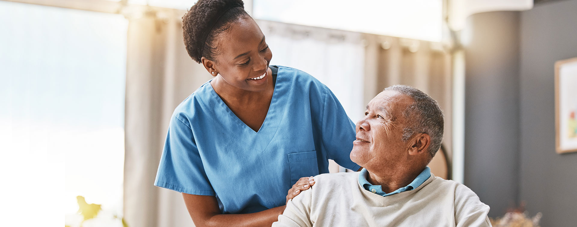 A caregiver providing after-surgery care in Beaumont, TX smiles at an older adult sitting in a wheelchair.